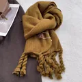 Detalle de bufanda de punto amarillo jengibre con borlas gruesas de estilo rústico - Bronceado