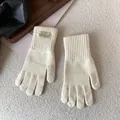 Close-up of cream-colored knit gloves with ribbed cuffs and embroidery on plush background - Ivory