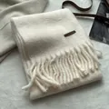 Détail de l'écharpe crème avec texture laineuse, franges et étiquette décorative - Crème