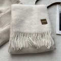 Detalle de bufanda de lana blanco crudo con textura suave, flecos y etiqueta de cuero - 180x30cm / Marfil