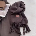 Detalle de bufanda de punto marrón oscuro con flecos largos y etiqueta de marca de alta gama - Café