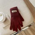 Close-up of deep red knit gloves with ribbed cuffs and branded woven label on a textured seat - Ancorra Red