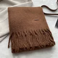 Close-up of dark brown wool scarf with thick tassels and premium leather label detail - Caramel Brown
