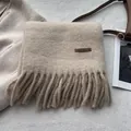 Close-up of beige knit scarf texture with fringe detail and brown leather brand label - Milky Apricot
