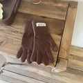Close-up of winter knitted gloves in dark brown with branded woven cuff label on wood - Coffee