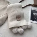 Detalle de la bufanda de punto crema con pompones esponjosos y una etiqueta de marca marrón - Blanco gardenia
