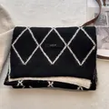 Detalle de bufanda de punto con cuadros y etiqueta de marca sobre tela suave - Crema Beige y Negro