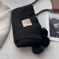 Detail of black faux cashmere scarf featuring plush pom-poms and minimalist woven label - Elegant Black