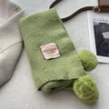 Detail of green knitted scarf with pom-pom trim and Vegetable House brand label - Creamy Green