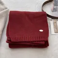 Dettaglio di sciarpa in maglia rosso scuro con logo in metallo e etichetta in legno - Rosso