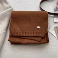 Dettaglio di sciarpa in maglia a coste caramello con logo in metallo argento e texture morbida - Arancione