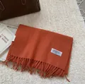 Detail of caramel pure wool scarf featuring long tassels and woven brand label - 180x30cm / Bright Orange