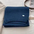 Close-up of navy blue knit texture with metal brand tag and cedar wood accessory - Sky Blue