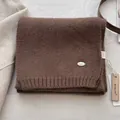 Detail of soft dark brown wool knit scarf with silver metal logo and wooden tag - Coffee
