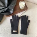 Close-up of black knitted gloves with ribbed cuffs and branded tag on soft background - Black