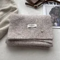 Detail of wool-blend oatmeal knitted scarf featuring a white woven label and metal buckle - Milk Tea Camel
