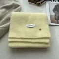 Detail of soft beige wool knit scarf featuring vertical ribbed texture and woven label - Light Yellow