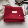 Close-up of red wool-blend scarf with a white label and a small golden metal charm - Christmas Red