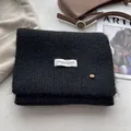 Detail of soft black wool knit scarf featuring white woven label and brown button detail - Black