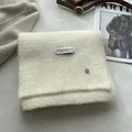 Detail of cream wool knit scarf featuring a branded fabric label and metal button detail - Ivory