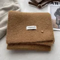 Macro detail of soft brown wool-blend knitted scarf with woven label and gold metal buckle - Dark Khaki