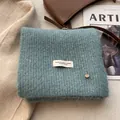 Close-up of grey-blue wool knit scarf with fashion label and gold metal charm detail - Lake Green