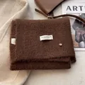 Detail of dark brown wool knit scarf with fluffy texture and white woven label - Caramel color