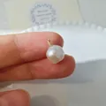 Primer plano de colgante de perla barroca artesanal con alambre de oro en la mano - Colgante de Perla Redonda