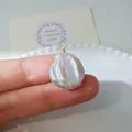 Detalle macro de un colgante de perla barroca con alambre dorado sostenido en el dedo - Colgante de Perla Plana