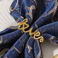 Macro detail of golden metal Love napkin ring on dark blue textured fabric background - Gold