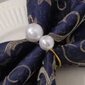 Elegante servilletero dorado con dos perlas blancas sobre servilleta azul oscuro - Dorado
