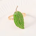 Dettaglio dell'anello portatovagliolo in smalto verde con venature dorate su piatto bianco - Design a foglia di pianta