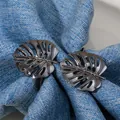 Close-up of metallic monstera leaf napkin rings in gunmetal finish on blue fabric - Black