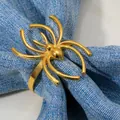 Golden spider napkin ring with a polished metallic finish on a light blue linen cloth - Gold