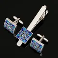 Detailopname van de zilveren dasspeld en manchetknopen met blauw bloemenpatroon - Zakelijke Manchetknopen Stropdasclip Driedelige Set