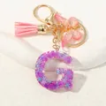 Dettaglio portachiavi lettera G in resina viola con paillettes, nappa e farfalla rosa - Alfabeto G (D1414-G)