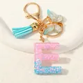 Close-up of glitter resin letter E keychain with blue tassel and gold butterfly - Letter E (D1417-E)