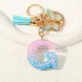 Close-up of resin letter G keychain with pink sequins, blue tassel and golden butterfly - Letter G (D1417-G)
