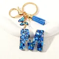 Letter M resin keychain with blue stones, gold flakes, tassel and butterfly charm - Letter M (D1413-M)