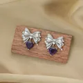 Titanium steel bowknot heart earrings with purple zircon on a warm satin background - Earrings / Silver