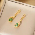 Detailed shot of peacock drop earrings with green teardrop stones on jewelry box - Gold Earrings