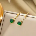 Detailed close-up of emerald green zircon gold earrings on champagne silk background - Stud Earrings / Gold