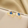 Detail of luxury gold stud earrings with oval blue stone and shimmering crystal halo - Gold Stud Earrings