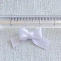 Detail shot of a 2.5cm white satin ribbon bow with ruler showing size for DIY crafts - White