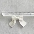 Close-up of a 3cm white satin ribbon bow accessory with ruler for size measurement - White