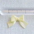 Macro shot of a small beige satin ribbon bow next to a ruler for precise size measurement - Beige