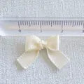 Macro view of a 2.5cm cream satin ribbon bow with ruler showing precise DIY craft dimensions - Milky White