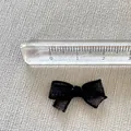 Macro detail of a small black mesh bow accessory with ruler showing 2cm width - Black