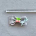 Detail einer grauen Satinschleife mit weißem Spitzenbesatz und rosa Fruchtanhänger - Grauer Stil