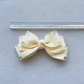 Detailed view of cream bow accessory with rhinestones next to a measuring ruler - Off White